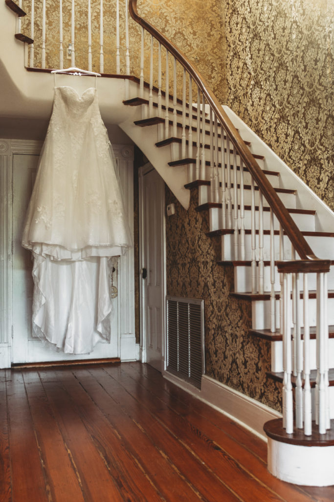 Bride's wedding dress hanging on the banister of the stair rail at Englund Estate Venue in Georgia. 