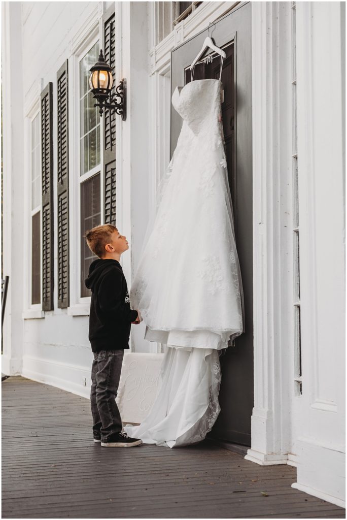 boy looking at wedding dress hanging on the door of the front porch of Englund Estate Venue in Georgia 