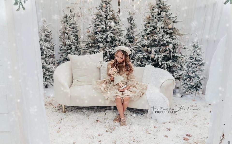 Christmas mini session. Little girl dressed in a formal dress, sitting on a white couch and flocked Christmas trees. 