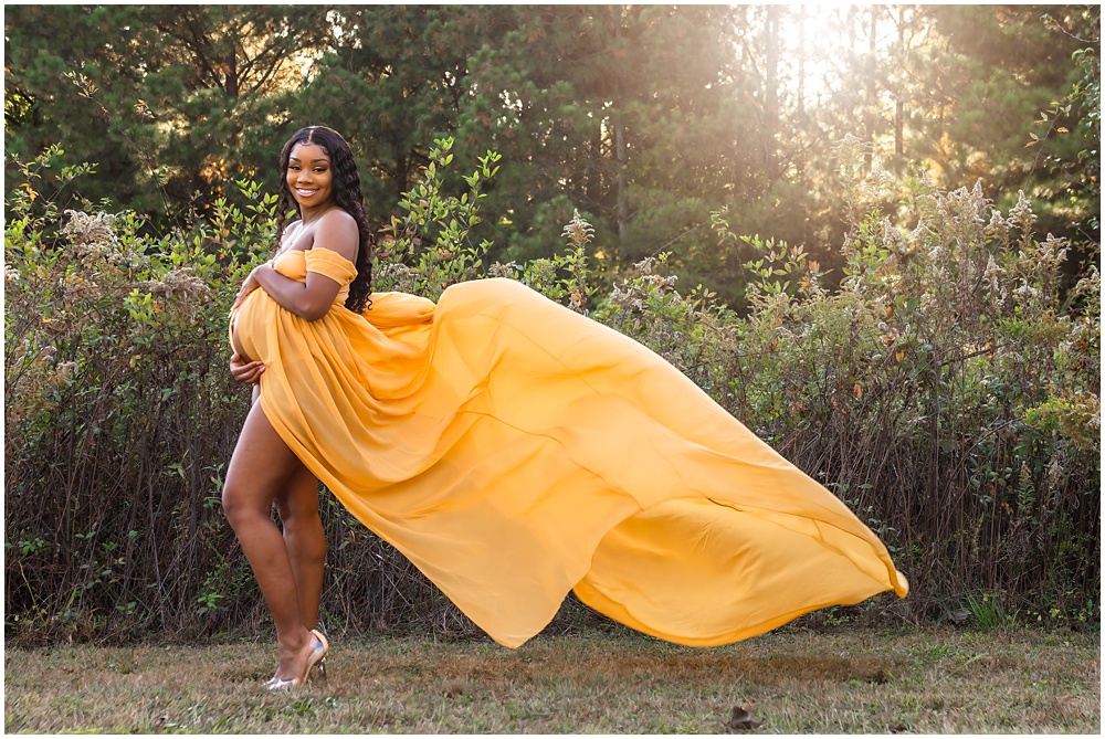 maternity session in roswell. mom to be wearing a bright yellow dress standing outside infront of tall bushes