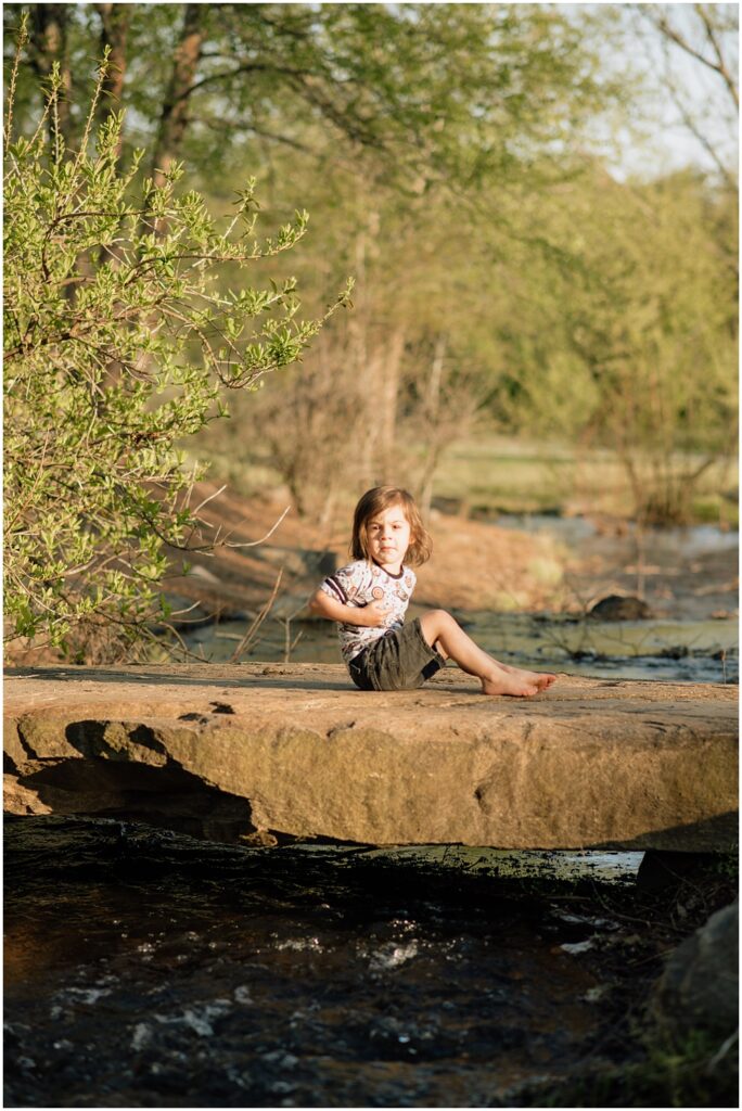 little boy sitting on a rock over a creek during his mommy and me session at Gerrard landing park. 