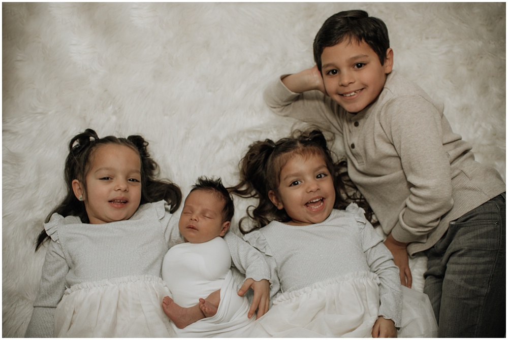 Flowery Branch photographer has a newborn baby in the studio. The newborn is surrounded by his siblings.