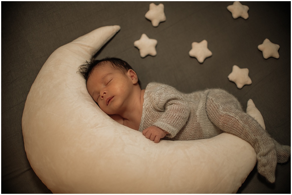 Flowery Branch photographer takes photo of the baby with props during the newborn session in the studio. Baby is laying in between the moon and stars.