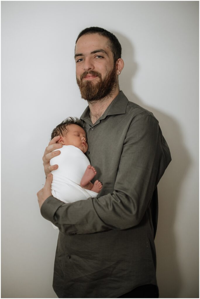 Flowery Branch photographer takes photo of the baby and his dad during the newborn session in the studio. Everyone is all smiles.